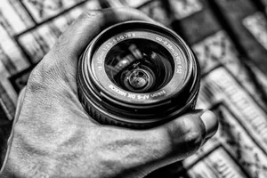 Black and white image of a Nikon camera lens being held, showcasing classic photography equipment. jigsaw puzzle
