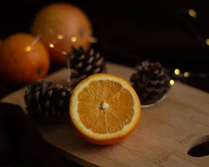 A halved orange displayed on a cutting board with pine cones in a dimly lit setting. jigsaw puzzle