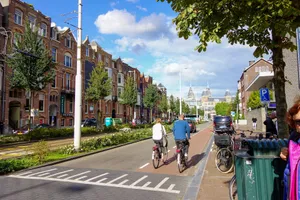 Two cyclists on a city street with buildings and trees. jigsaw puzzle