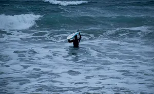 person in black wet suit holding white surfboard on sea waves during daytime jigsaw puzzle