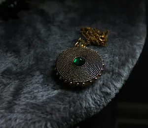 A gold pendant with a green gem rests on fur. jigsaw puzzle