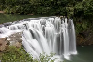 Beautiful cascading waterfall surrounded by dense greenery, captured in daylight. jigsaw puzzle
