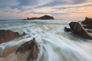 Capture of ocean waves crashing against rocks at sunset, showcasing serene coastal scenery. jigsaw puzzle