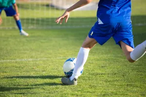 A young soccer player in blue uniform kicks a ball towards the goal on a sunny day. jigsaw puzzle