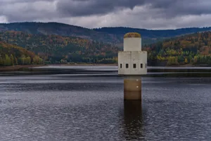 A concrete intake tower stands in a tranquil reservoir surrounded by lush autumn forests. jigsaw puzzle