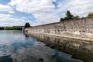 Serene view of the Möhne Reservoir dam wall, surrounded by nature under a partly cloudy sky. jigsaw puzzle