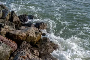 Close-up of rugged rocks on a coastline with waves crashing, depicting nature's power and beauty. jigsaw puzzle