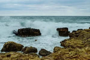 Dramatic view of ocean waves crashing on rocks at the shoreline under a cloudy sky. jigsaw puzzle