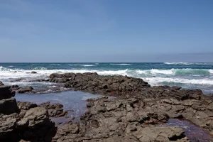 Stunning view of rocky shoreline with crashing waves under a clear blue sky. jigsaw puzzle