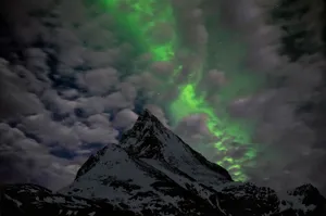 Stunning view of the Northern Lights illuminating the night sky above a snow-covered mountain peak. jigsaw puzzle