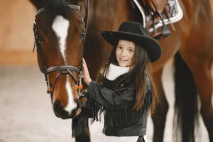A cheerful young girl in a cowboy hat bonding with a horse indoors. jigsaw puzzle