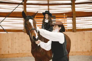 An elderly man assists a young girl on horseback inside a stable. Both wear cowboy hats. jigsaw puzzle