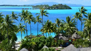 Scenic view of a tropical island with palm trees, turquoise ocean, and distant huts. jigsaw puzzle