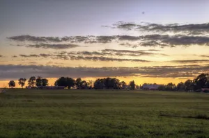 A tranquil rural landscape with expansive farmland and a beautiful sunset sky. jigsaw puzzle