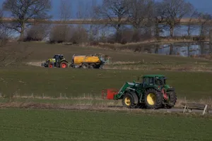 Two tractors operating in a picturesque rural field near a lake under clear skies. jigsaw puzzle