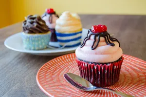 Close-up of assorted cupcakes with icing and cherry on colorful plates, perfect for dessert lovers. jigsaw puzzle