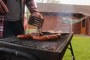 Grilling sausages and patties in a backyard with a rustic wooden house in the background. jigsaw puzzle