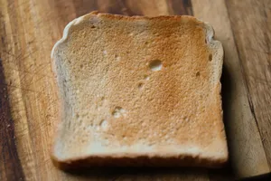 A detailed view of a single slice of toasted white bread on a wooden surface. jigsaw puzzle