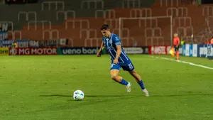 A soccer player in blue jersey dribbling the ball on a well-lit field during a night match. jigsaw puzzle