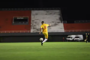 Soccer player in yellow jersey kicking a ball on a green pitch during night match under lights. jigsaw puzzle