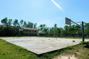 Empty outdoor basketball court surrounded by trees and an old building under the clear blue sky. jigsaw puzzle