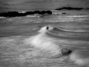 Silhouette of a lone surfer navigating waves in a dramatic black and white ocean scene. jigsaw puzzle