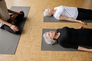 Two senior women practicing relaxation on yoga mats indoors, supervised by an instructor. jigsaw puzzle
