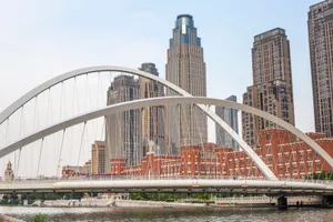 Suspension bridge over a river with skyscrapers in the background under sunlight. jigsaw puzzle