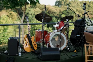 An outdoor stage setup with a drum set, guitar, and amplifier amidst greenery. jigsaw puzzle