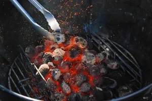 Close-up of hot, glowing charcoal briquettes in a grill, with tongs stirring embers. jigsaw puzzle