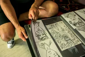 A person wearing shorts and sneakers turning pages of a comic art album, with close-up on hands and drawings. jigsaw puzzle