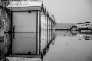 A serene black and white photo capturing boat garages and boats reflecting on calm water. jigsaw puzzle