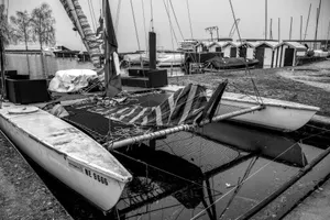 A black and white image of a catamaran docked at a marina with nearby storage sheds. jigsaw puzzle