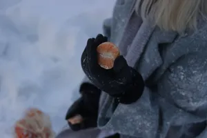 Close-up of a person holding a tangerine slice in winter gloves outdoors. jigsaw puzzle