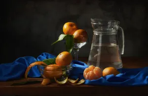 A still life composition featuring tangerines on a blue cloth beside a glass jug of water. jigsaw puzzle