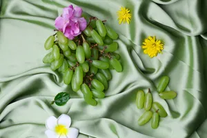 Elegant display of green grapes and colorful flowers on soft green silk fabric, perfect for luxurious themes. jigsaw puzzle