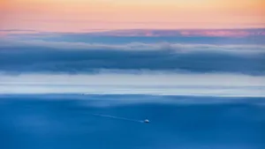 Serene aerial view of a ship sailing on the ocean under a colorful sunset sky. jigsaw puzzle